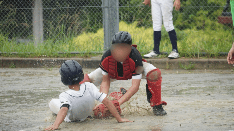 水たまりになったホームベースに滑り込む走者とタッチにいくキャッチャー