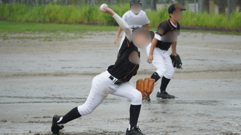 雨が降るぬかるんだマウンドで踏み込んで投げる少年野球のピッチャー